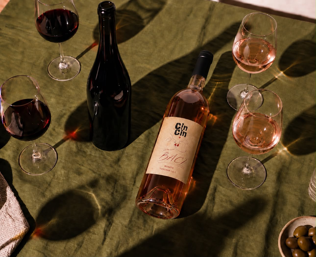 Calici di vino rosso e rosé CinCin Baci su tovaglia verde, illuminati dal sole