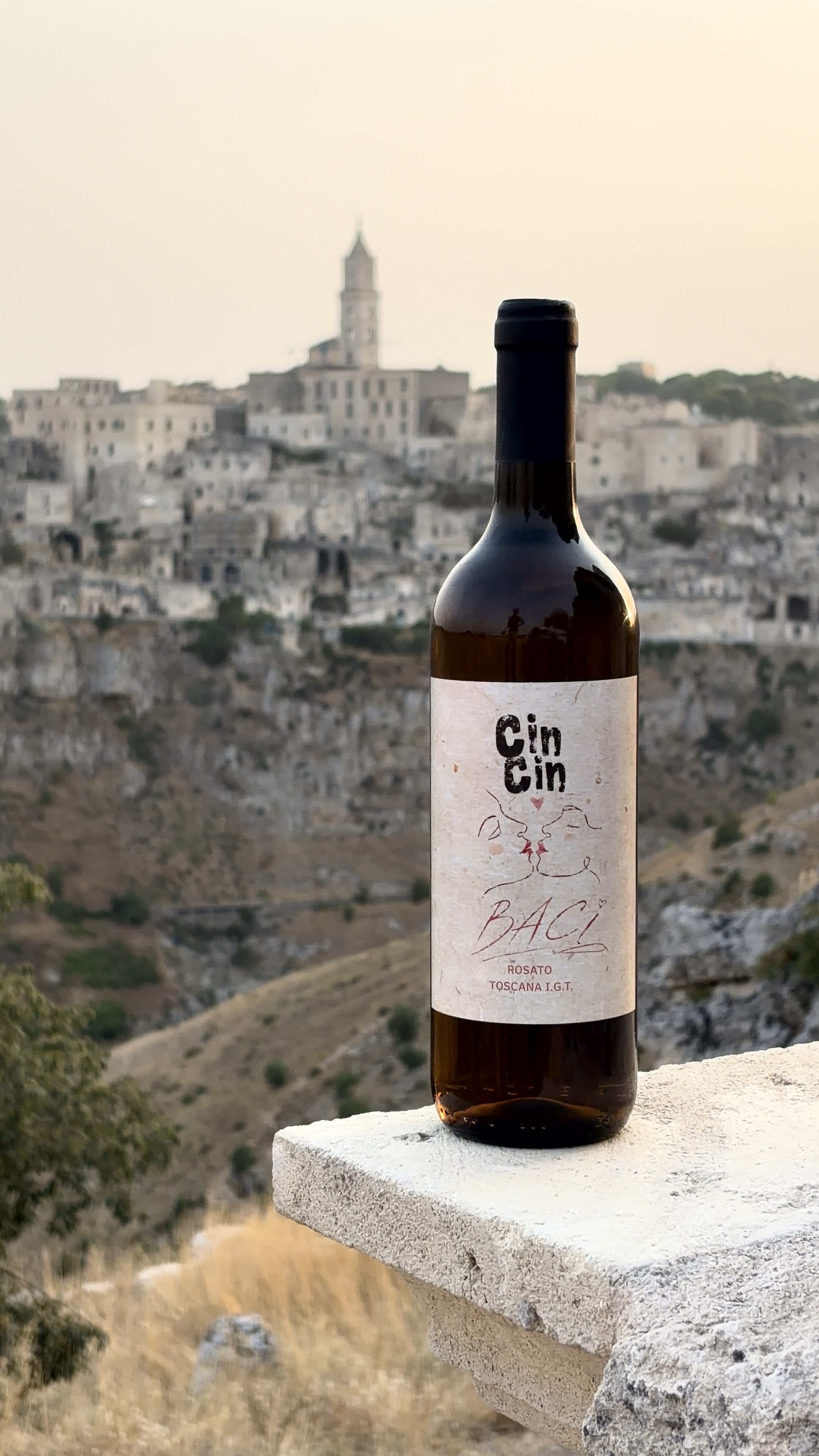 Bottiglia di CinCin Baci al tramonto, con un borgo italiano sullo sfondo